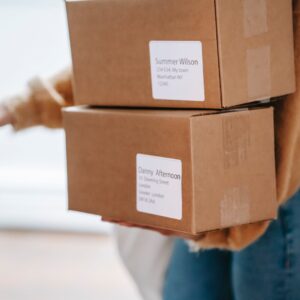 Crop unrecognizable woman carrying boxes and entering post office